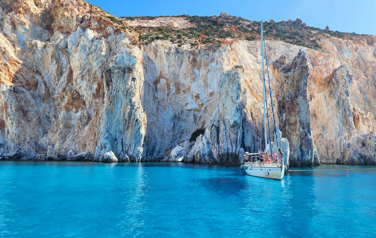 Sailing boat below white cliffs in turquoise Greek waters